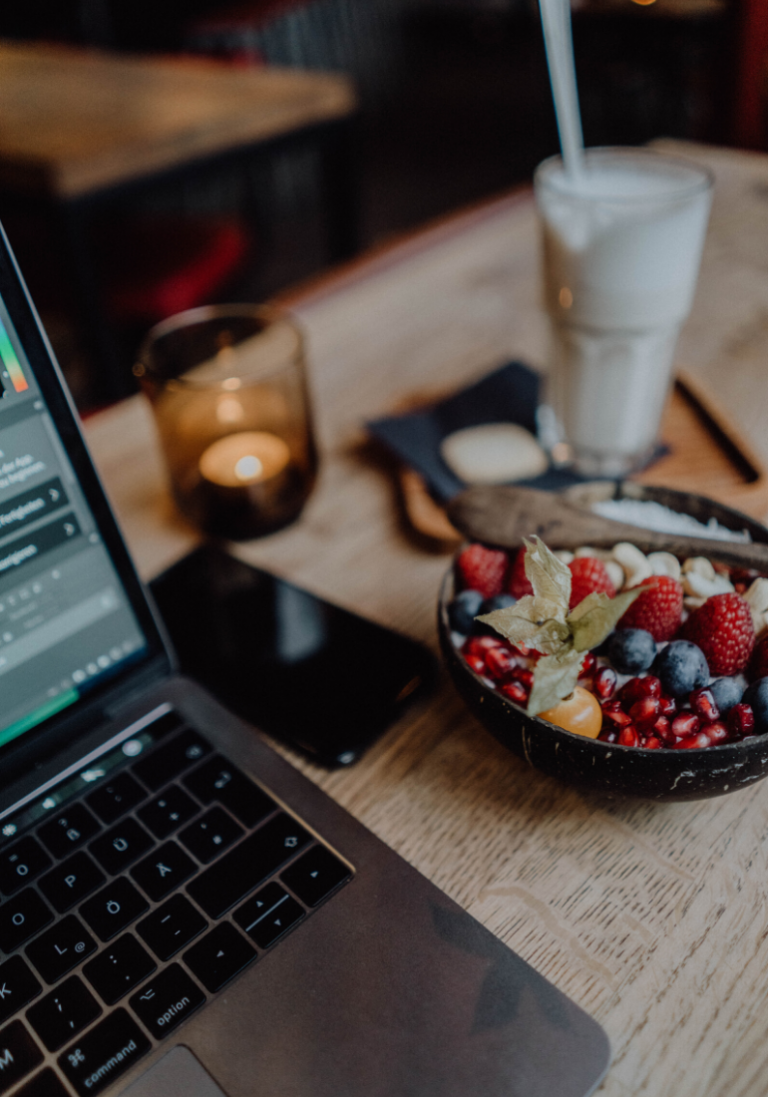 Sur cette photo, nous sommes dans un café. Sur la table, nous apercevons un ordinateur, un téléphone et des snacks.