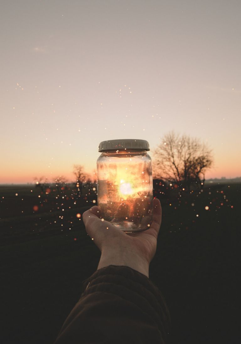 In this image, we see a hand holding an illuminated jar, capturing the sunset.