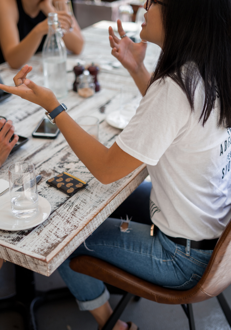 Sur cette image, on aperçoit une femme discutant avec ses collègues autour d'une table de restaurant.